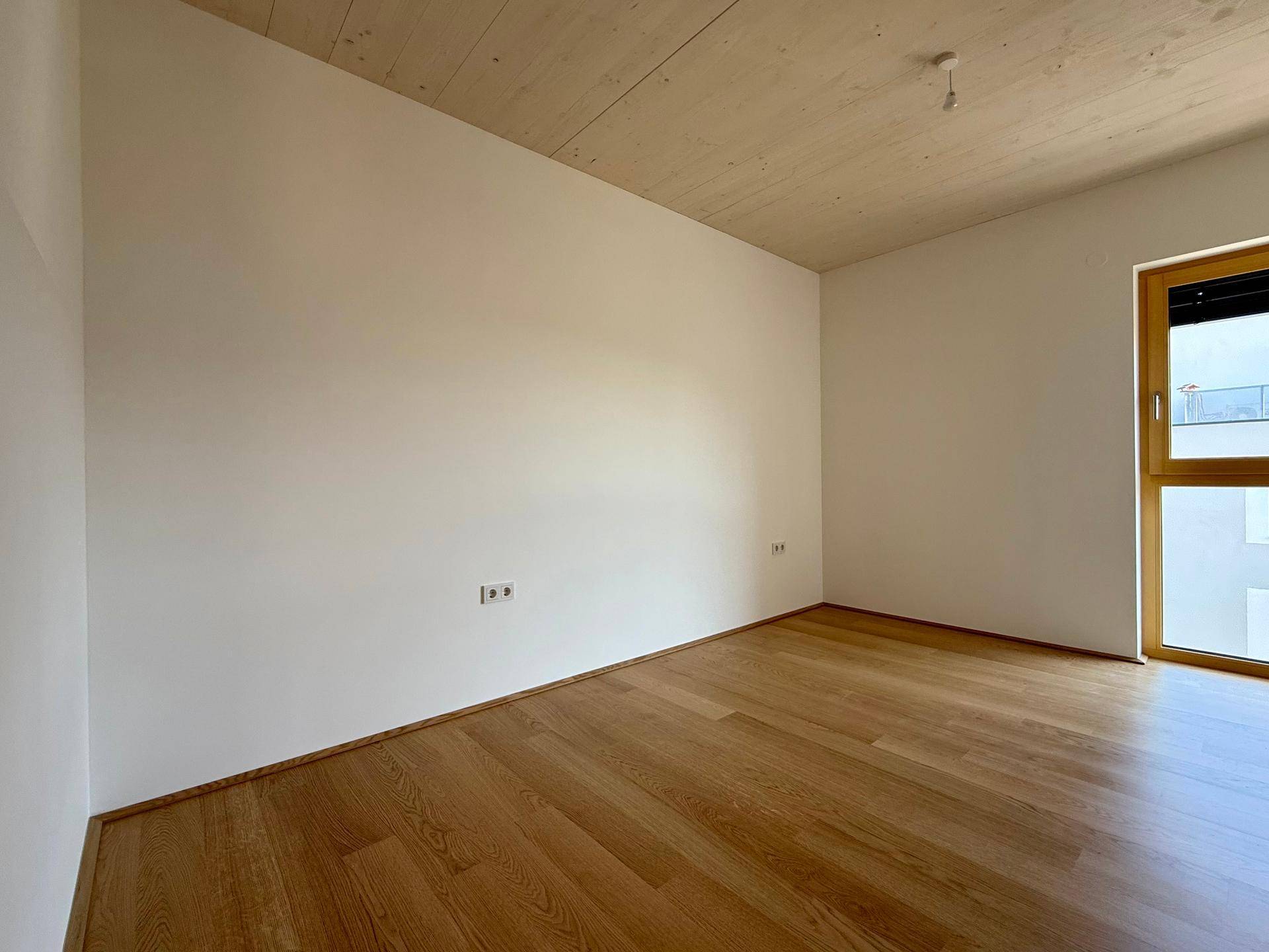 Helles Schlafzimmer mit Holzboden und Fenster, bereit zur individuellen Gestaltung.