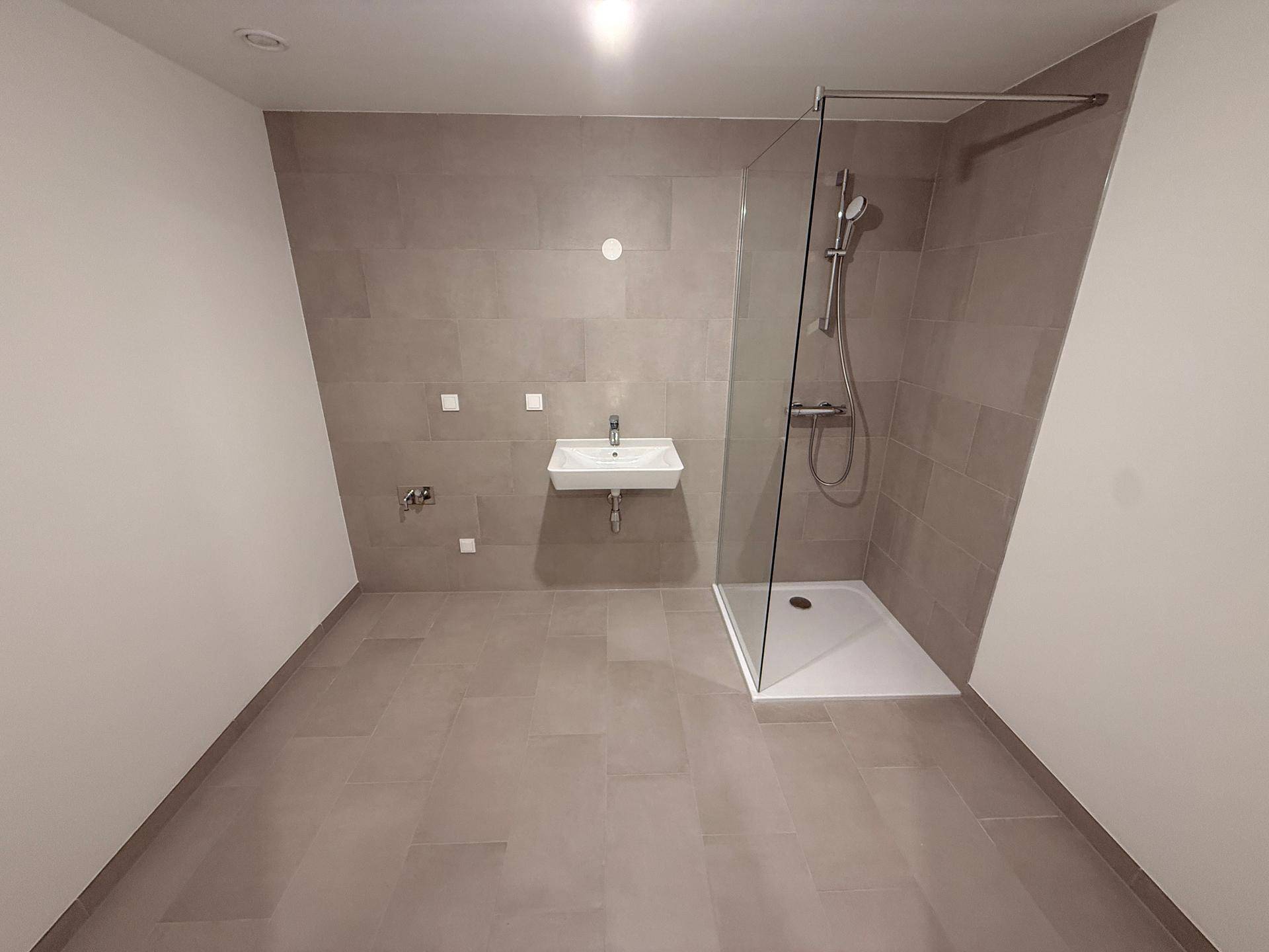 Geräumiges Badezimmer mit zeitgemäßer Ausstattung, großer Dusche und eleganten grauen Fliesen.