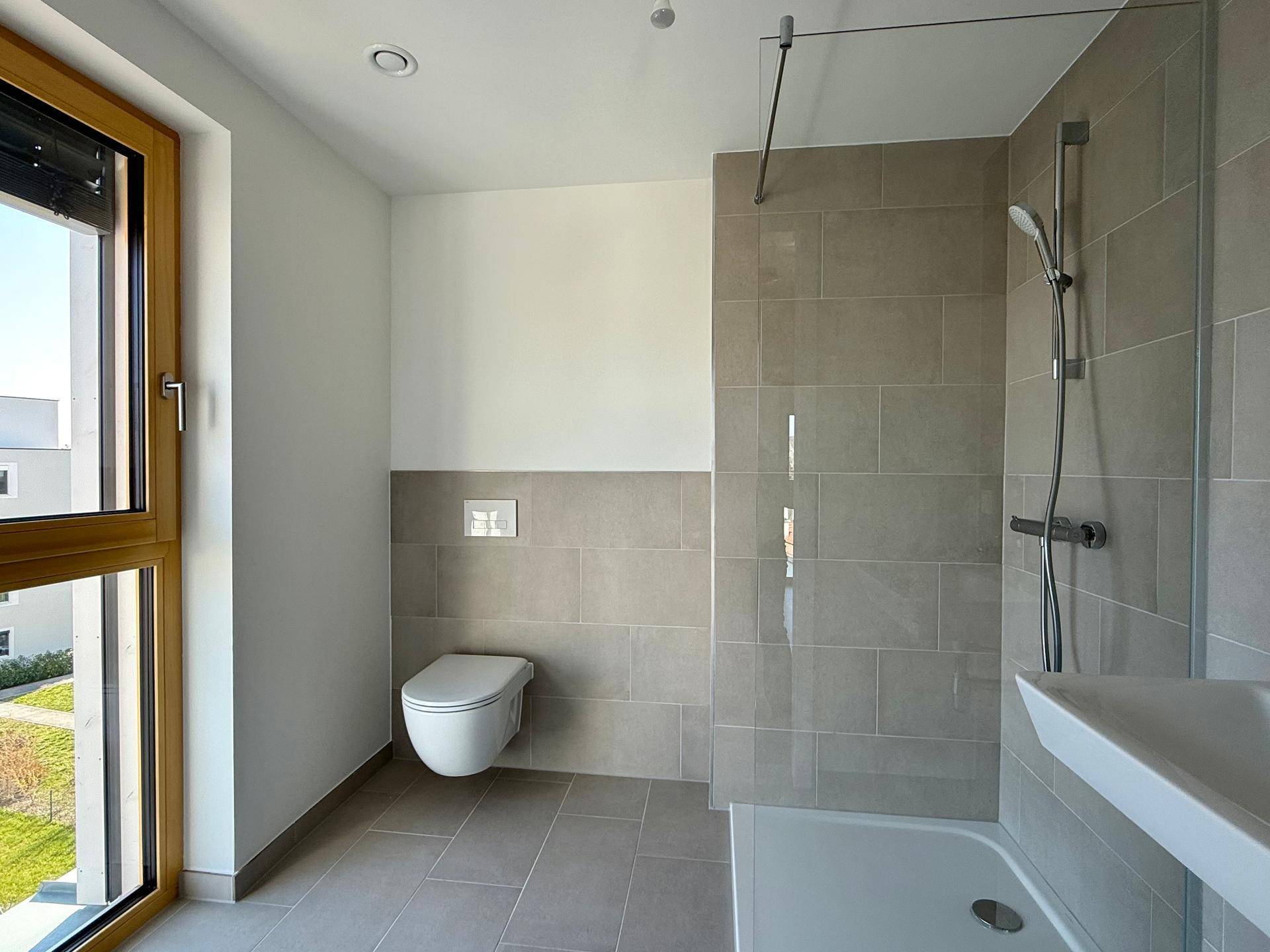 Modernes Badezimmer mit Dusche, WC, Waschbecken und einem Fenster für Tageslicht und Belüftung.