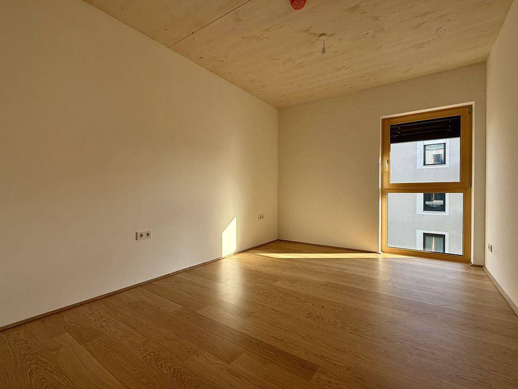 Helles Schlafzimmer mit Holzboden und großem Fenster, das viel Tageslicht hereinlässt.
