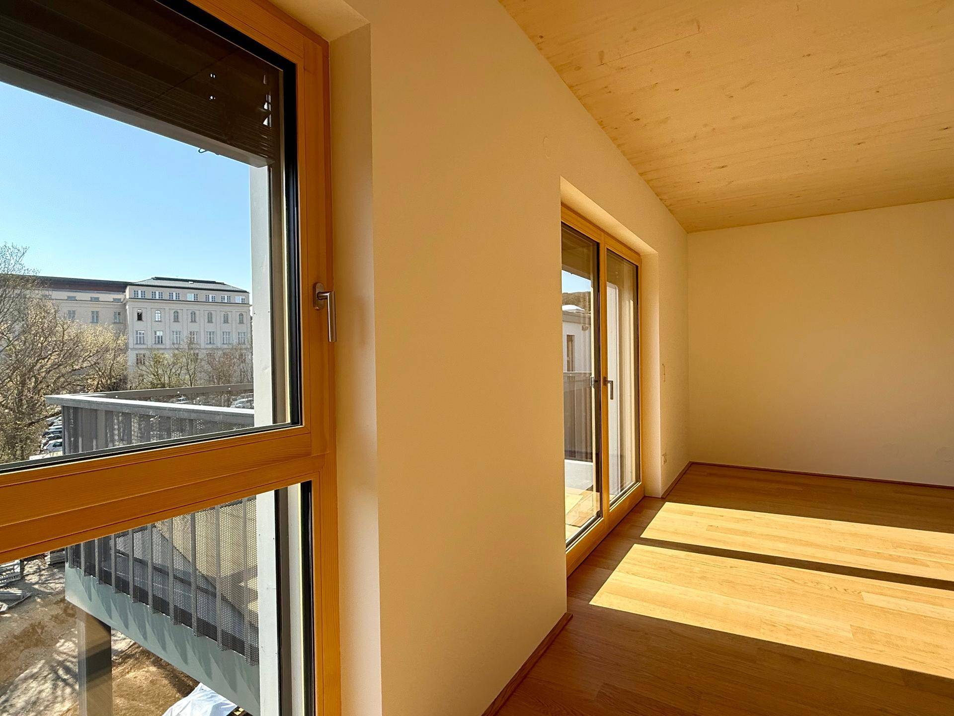 Heller Wohnraum mit Holzboden und Blick auf die umliegenden Gebäude durch große Fenster.