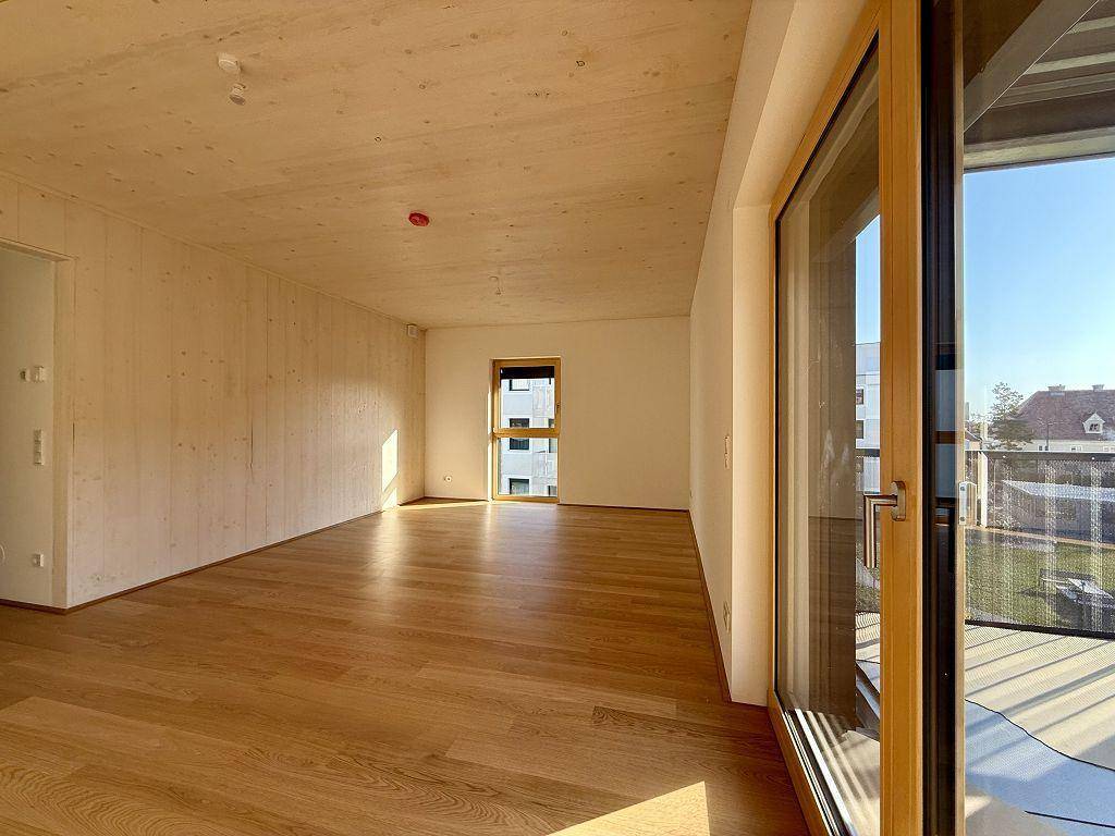 Heller Raum mit Holzboden und großem Fenster, das viel Tageslicht hereinlässt.