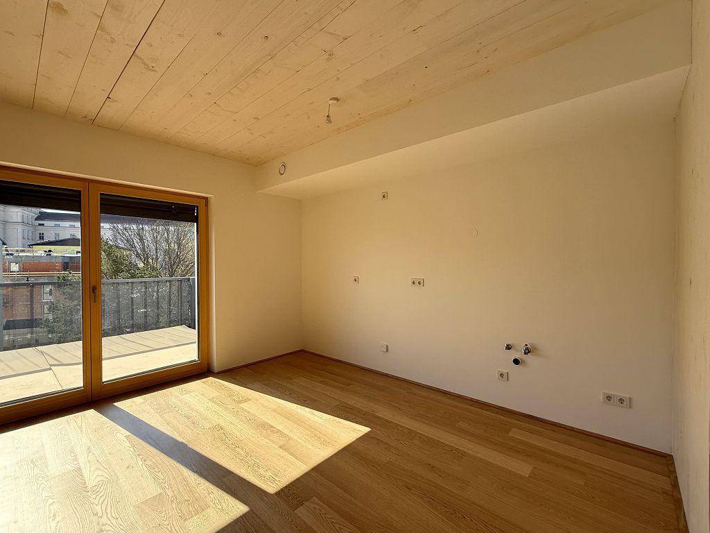 Geräumiger Raum mit Holzboden, Balkonzugang und vorbereiteten Anschlüssen für eine Küche.