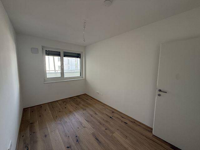 Helles Schlafzimmer mit Holzboden und Fenster, ausgestattet mit Außenjalousien für Privatsphäre.