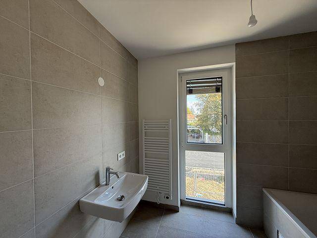 Modernes Badezimmer mit grauen Fliesen, einem einzelnen Waschbecken und einem Fenster für Tageslicht.