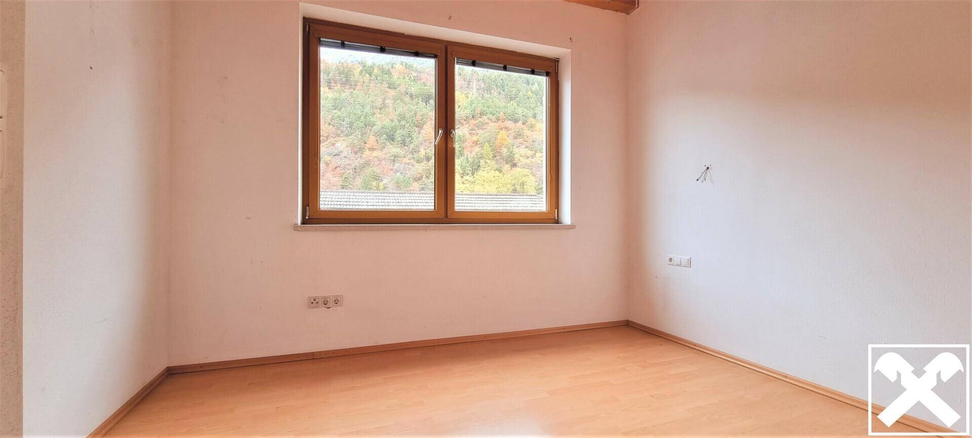 Helles Schlafzimmer mit Holzboden und Fenster mit Blick ins Grüne.