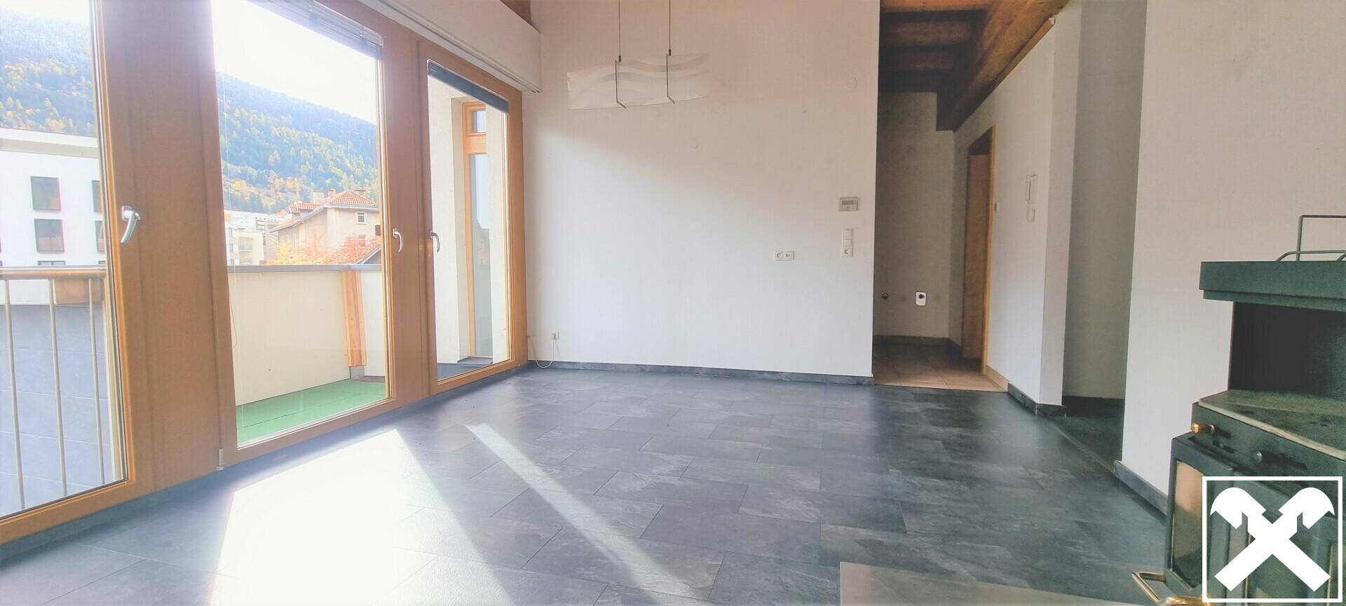 Geräumiges Wohnzimmer mit großen Fenstern, die viel Tageslicht hereinlassen und Zugang zum Flur.