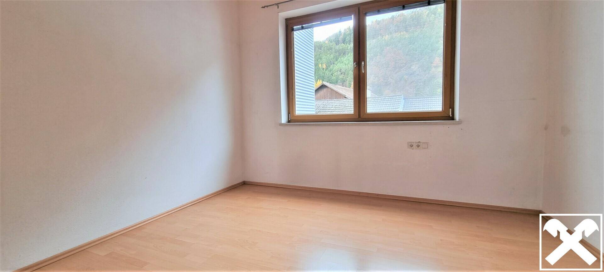 Ruhiges Schlafzimmer mit Holzboden und Fenster, das einen Blick auf die umliegende Natur bietet.