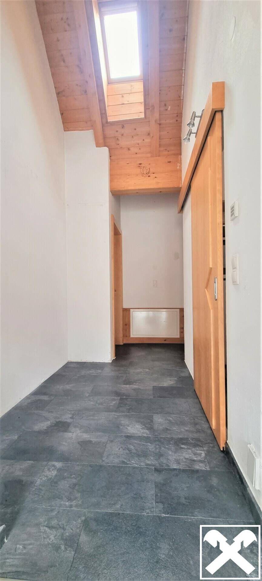 Heller Flur mit Holzbalkendecke, Fliesenboden und einem Dachfenster für natürliches Licht.