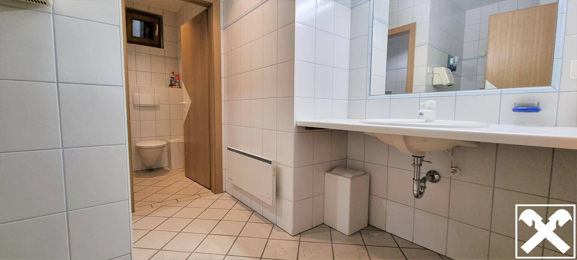 Helles Badezimmer mit weißen Fliesen, Toilette, Waschbecken und einem kleinen Fenster, das für Tageslicht sorgt.