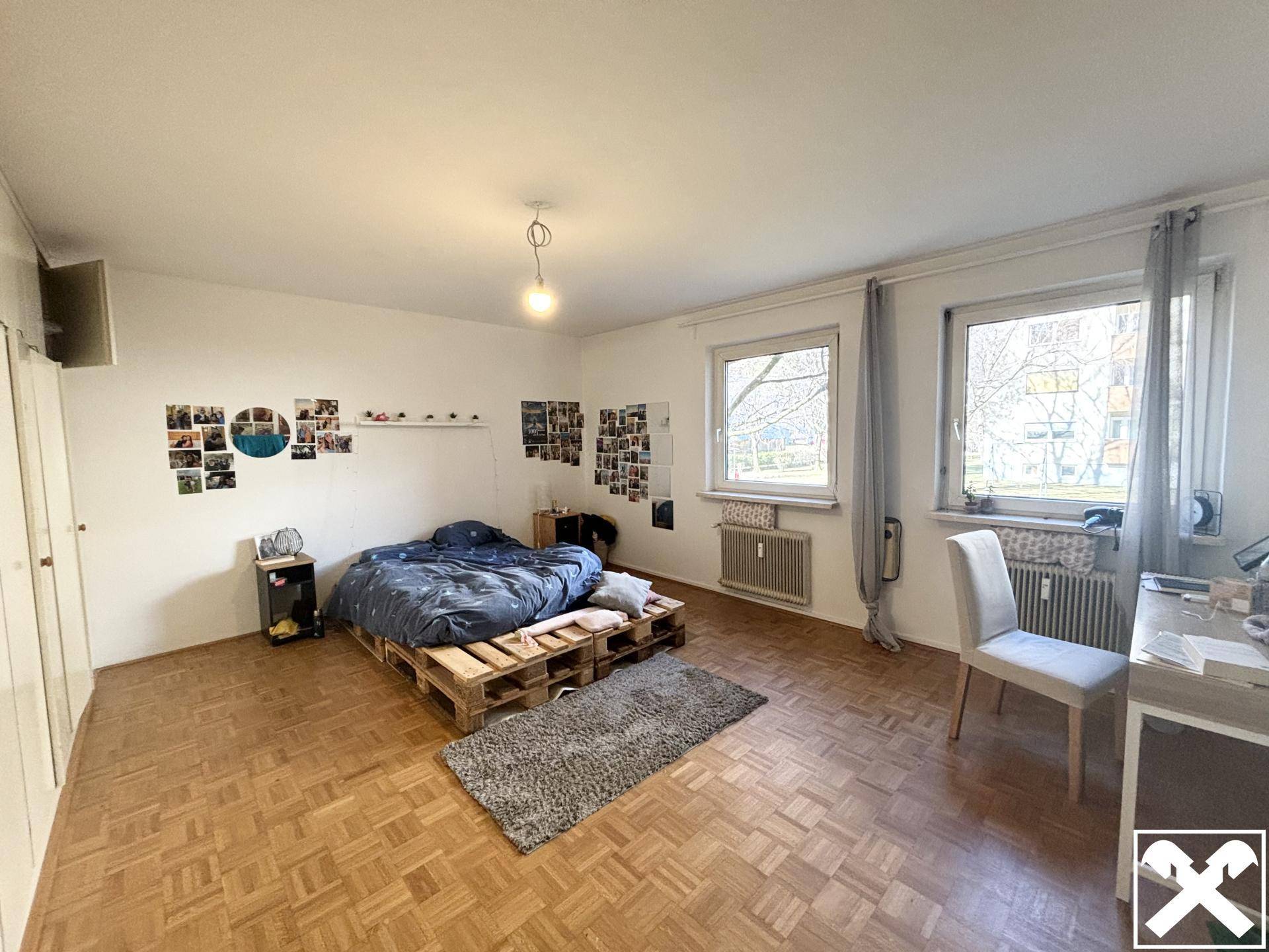 Helles Schlafzimmer mit Parkettboden, Palettenbett und großem Fenster mit Blick ins Grüne.