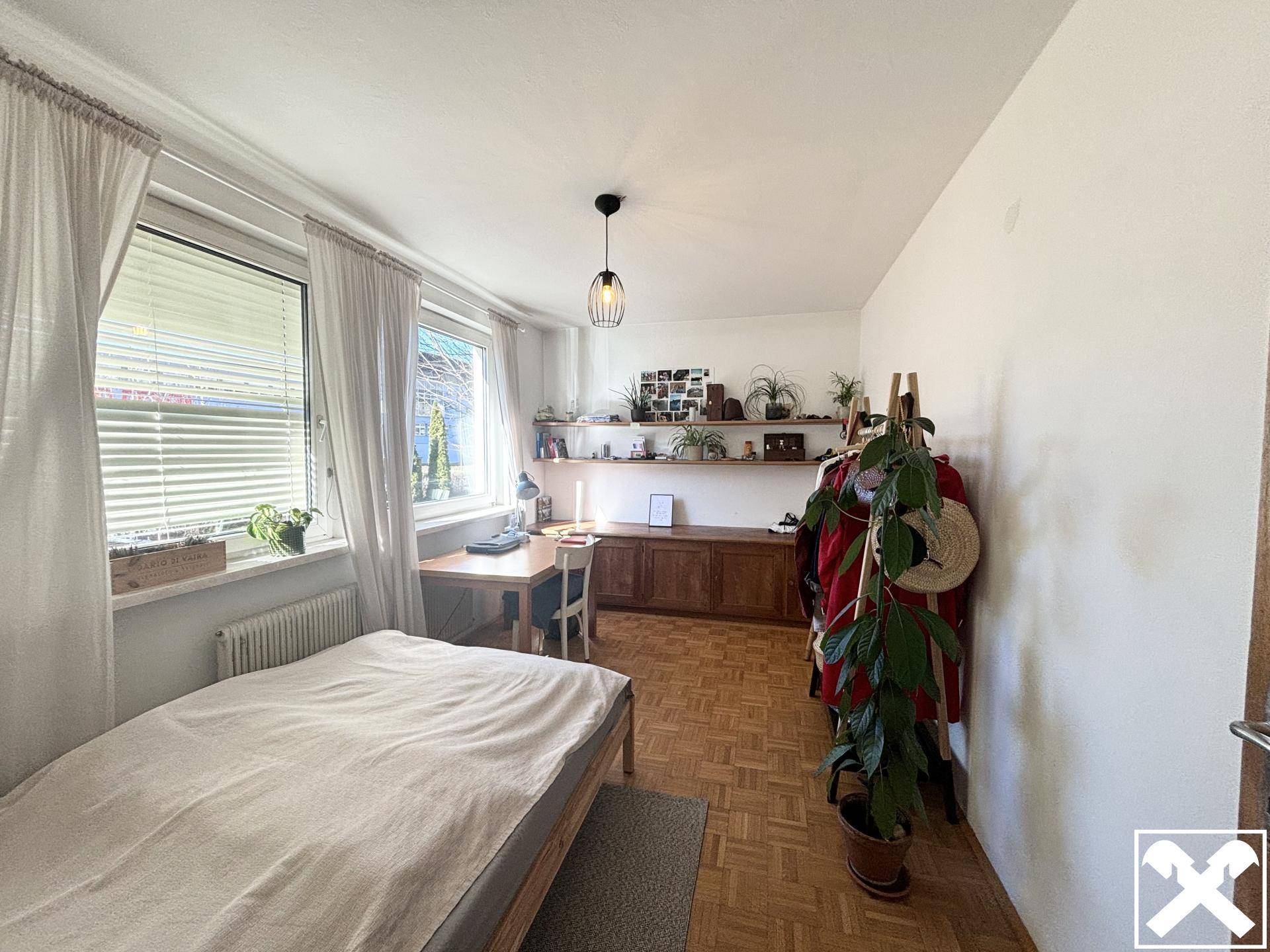 Gemütliches Schlafzimmer mit Parkettboden, Schreibtisch und Blick auf die grüne Umgebung.