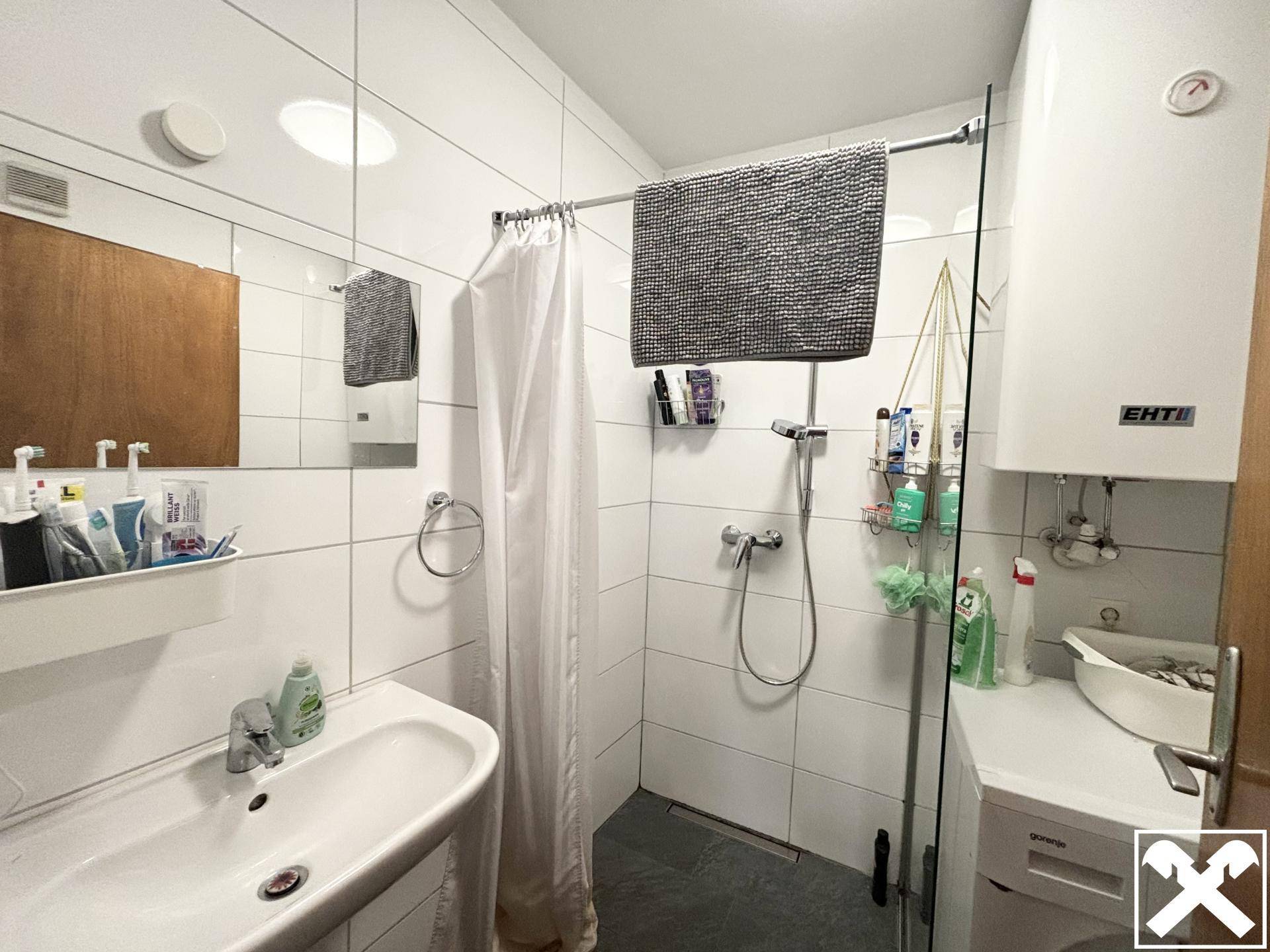Modernes Badezimmer mit Dusche, Waschbecken und Waschmaschine, hell gefliest.