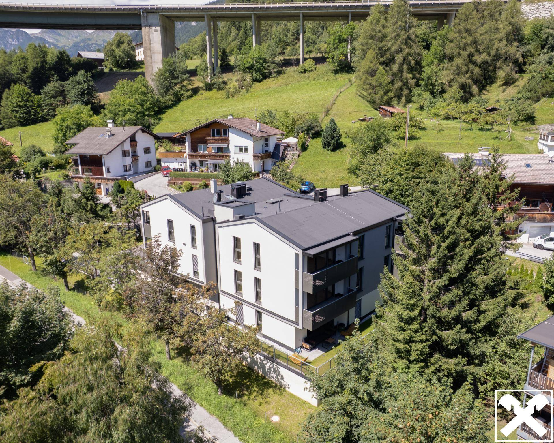 Luftaufnahme des modernen Wohngebäudes eingebettet in die grüne Landschaft mit Brücke im Hintergrund.