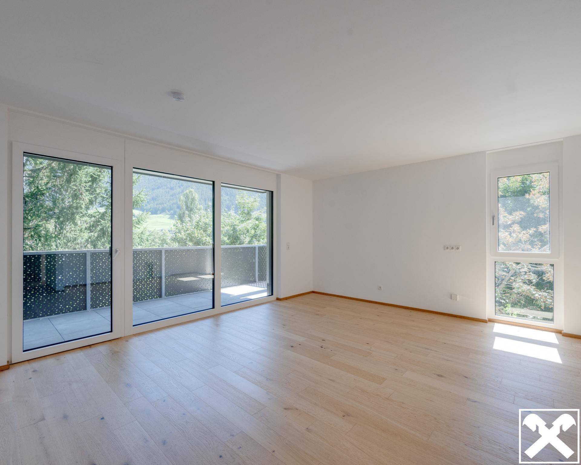 Helles Wohnzimmer mit großen Fenstern, Holzboden und Zugang zu einem Balkon mit Bergblick.