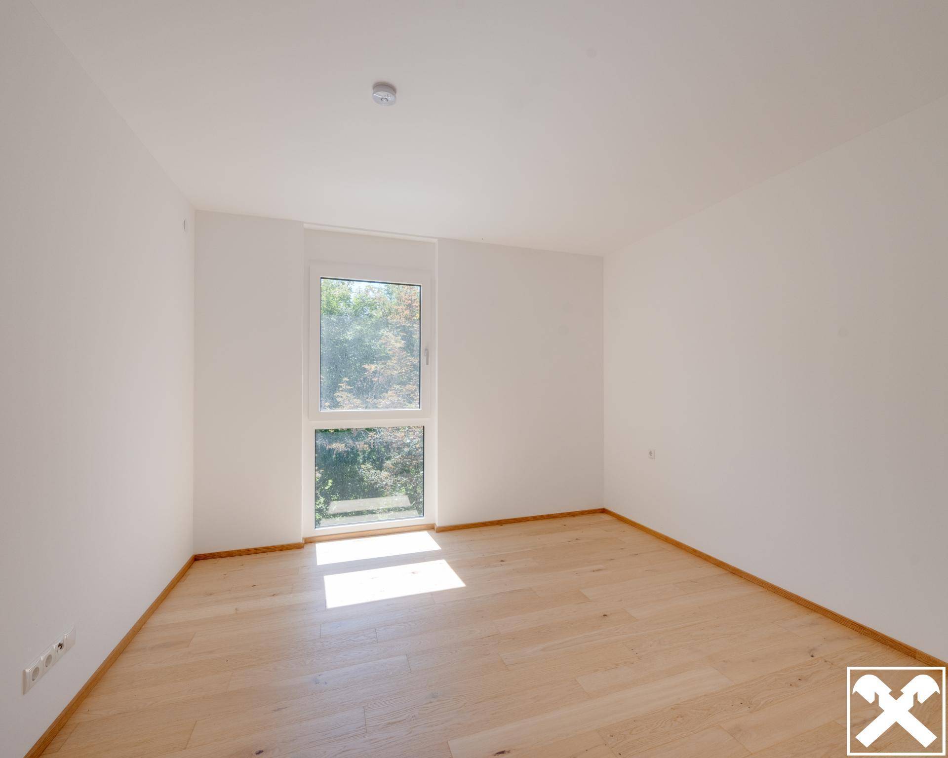 Ruhiges Schlafzimmer mit hellem Holzboden und einem großen Fenster mit Blick ins Grüne.