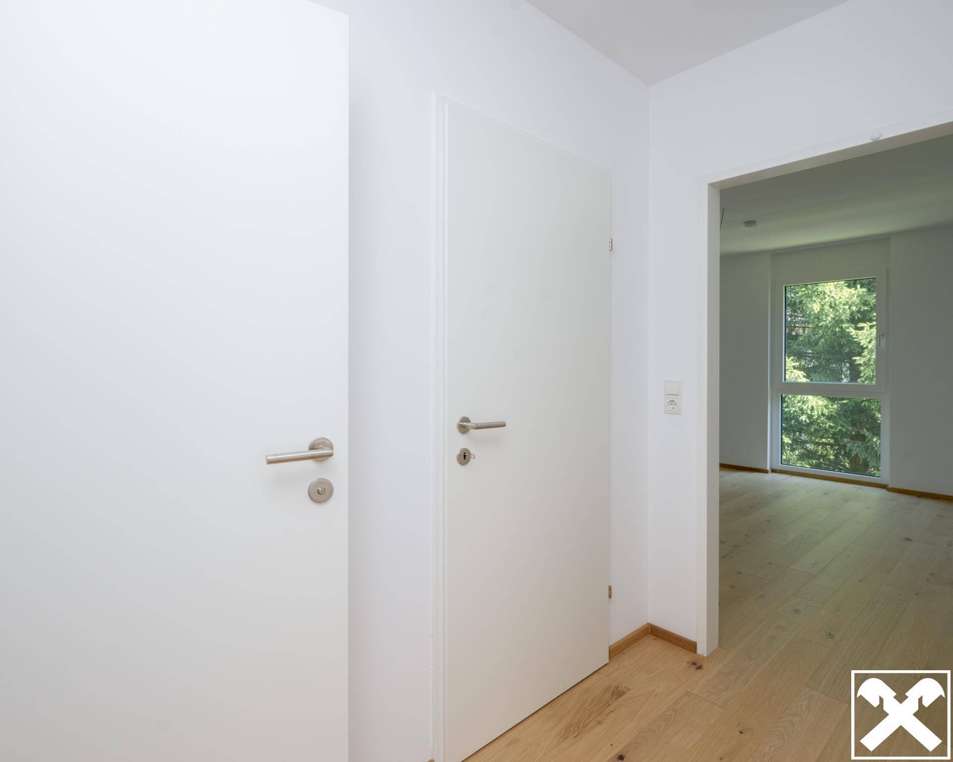 Heller Eingangsbereich mit weißen Türen und Holzboden, der zu den Wohnräumen führt.