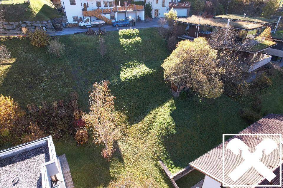 Großes grünes Grundstück zwischen Wohnhäusern mit einigen Bäumen und viel Sonnenlicht.