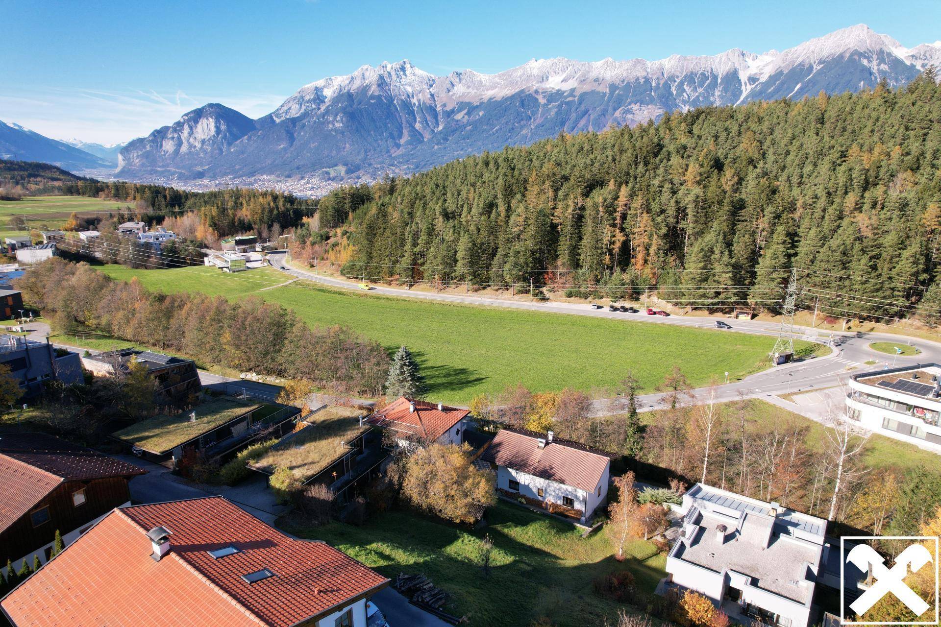 Weitwinkelaufnahme eines Wohngebiets mit Wald, Straße und majestätischen schneebedeckten Bergen im Hintergrund.