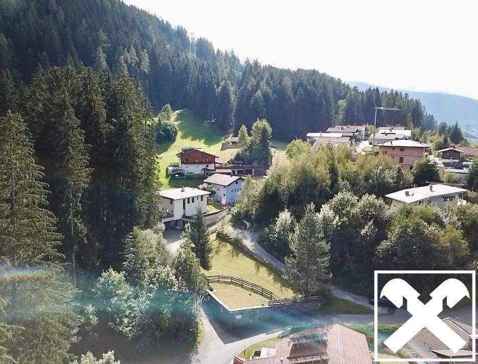 Weitläufige Luftaufnahme einer Siedlung eingebettet in eine bewaldete Berglandschaft.