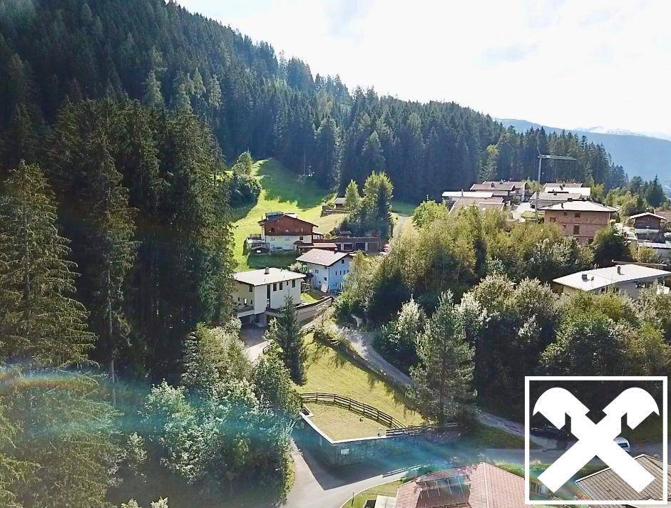 Weitläufige Luftaufnahme einer Siedlung eingebettet in eine bewaldete Berglandschaft.
