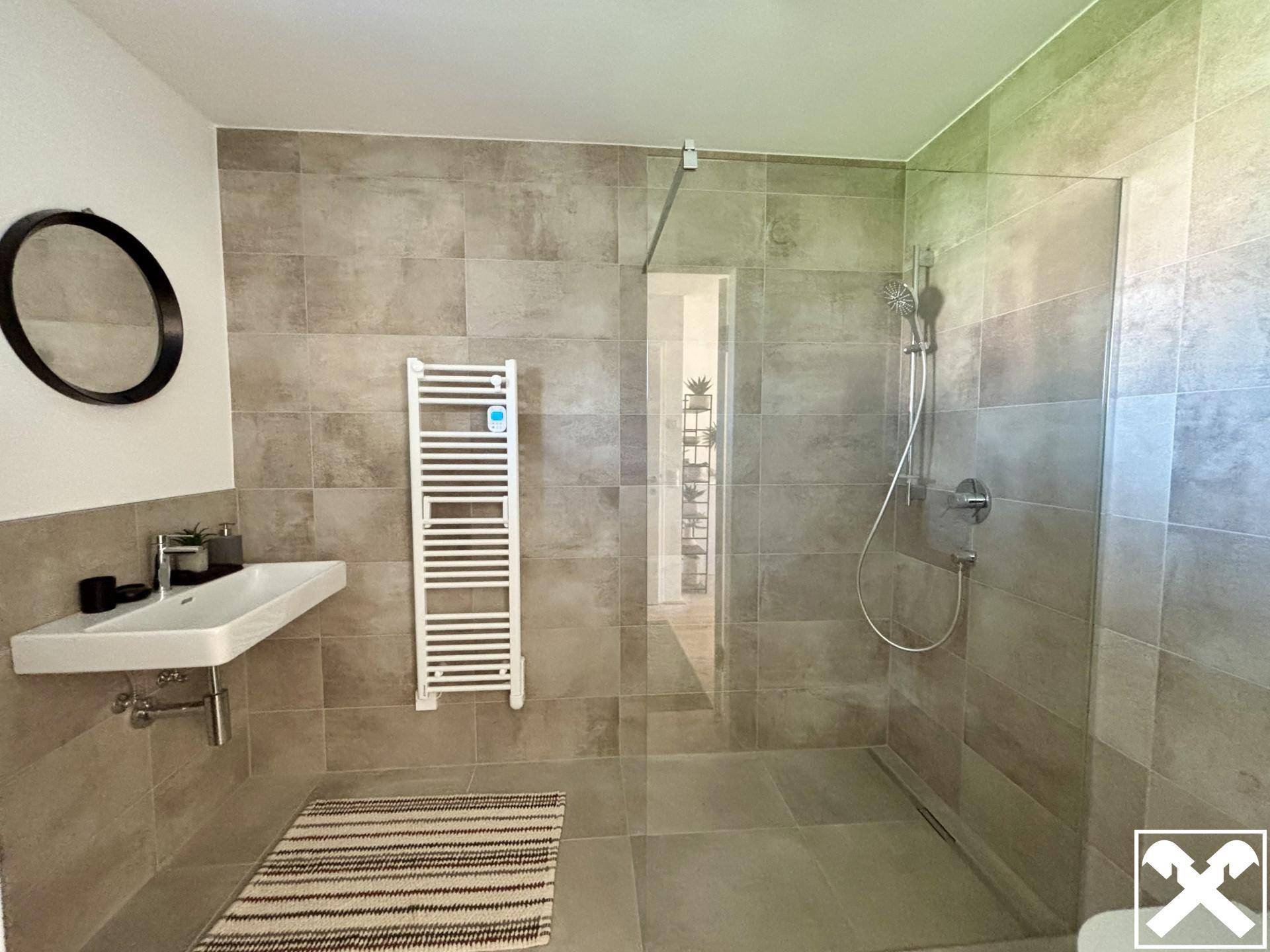 Modernes Badezimmer mit begehbarer Dusche, grauen Fliesen und beheiztem Handtuchhalter.