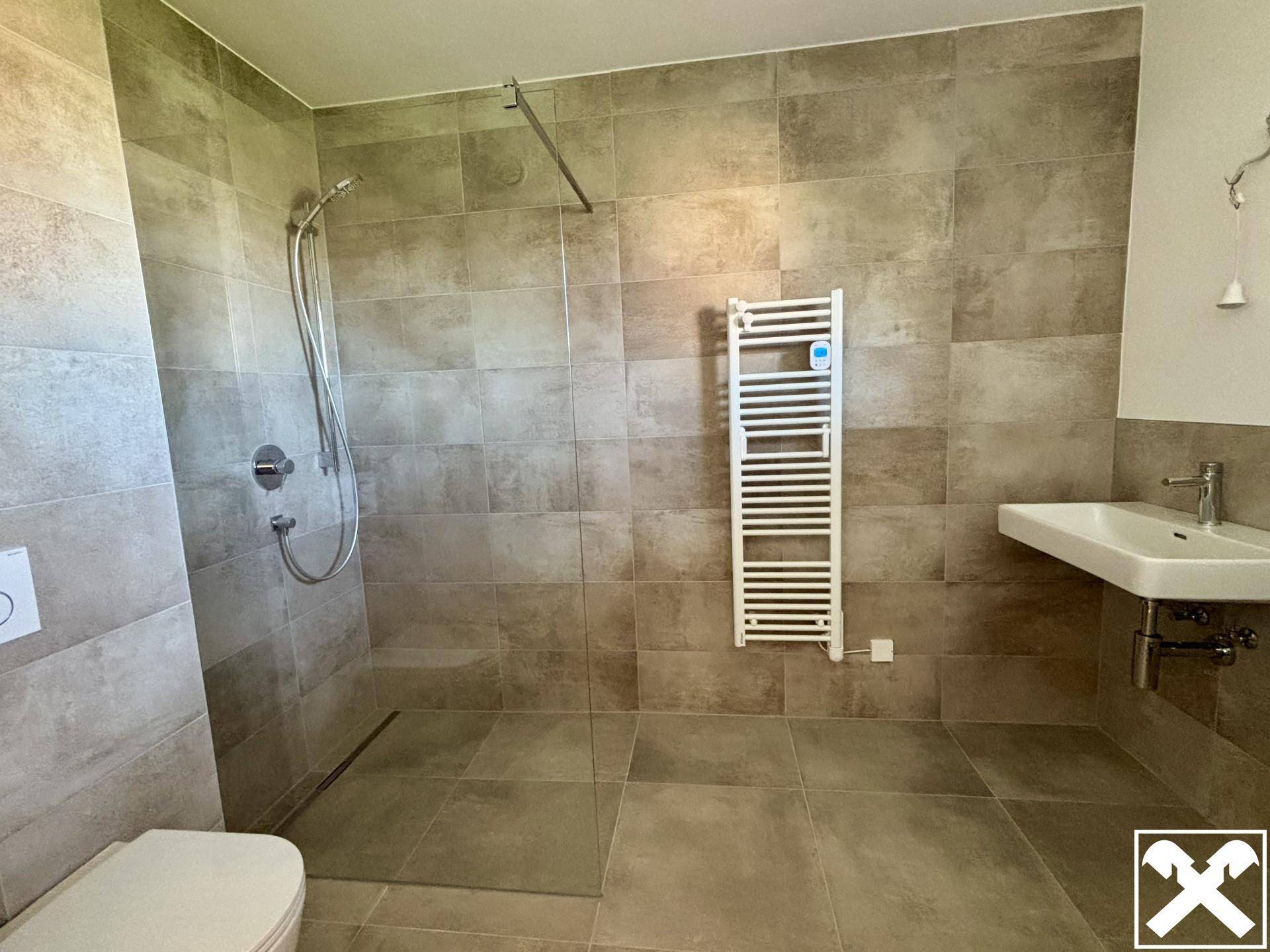 Modernes Badezimmer mit begehbarer Dusche, Wand-WC und praktischem Handtuchheizkörper.