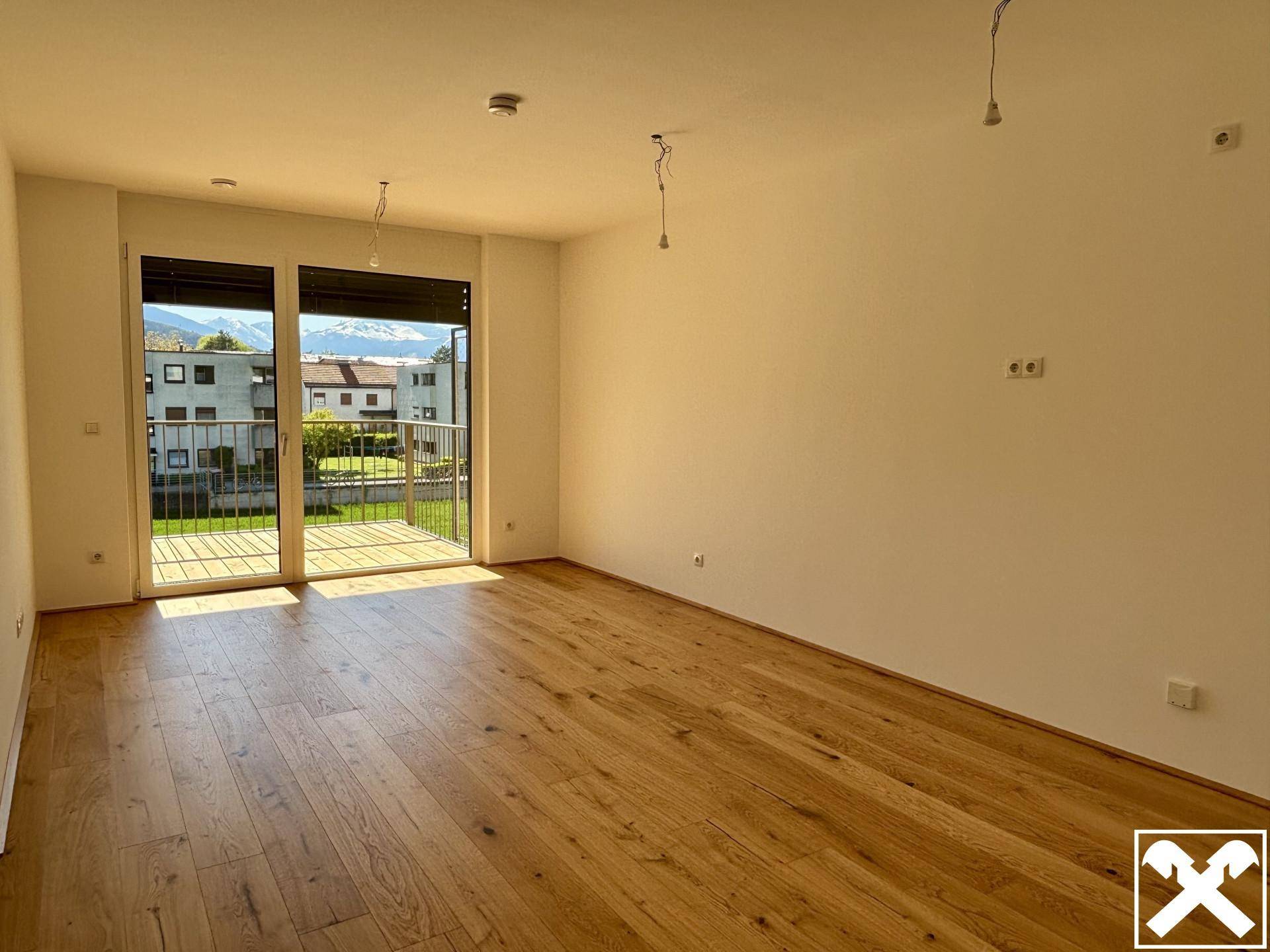 Heller Wohnraum mit Holzboden und Zugang zum Balkon, bietet einen weiten Blick auf die Berge.
