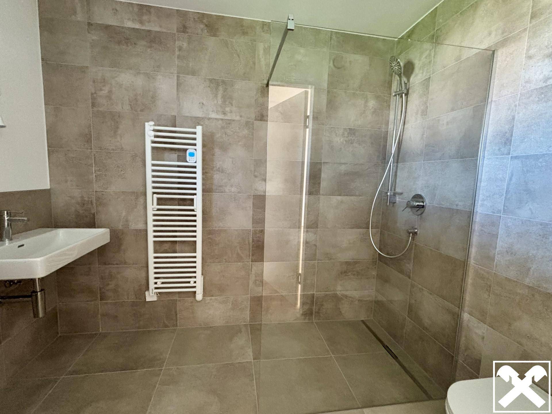 Modernes Badezimmer mit großformatigen Fliesen, ebenerdiger Dusche und beheiztem Handtuchhalter.