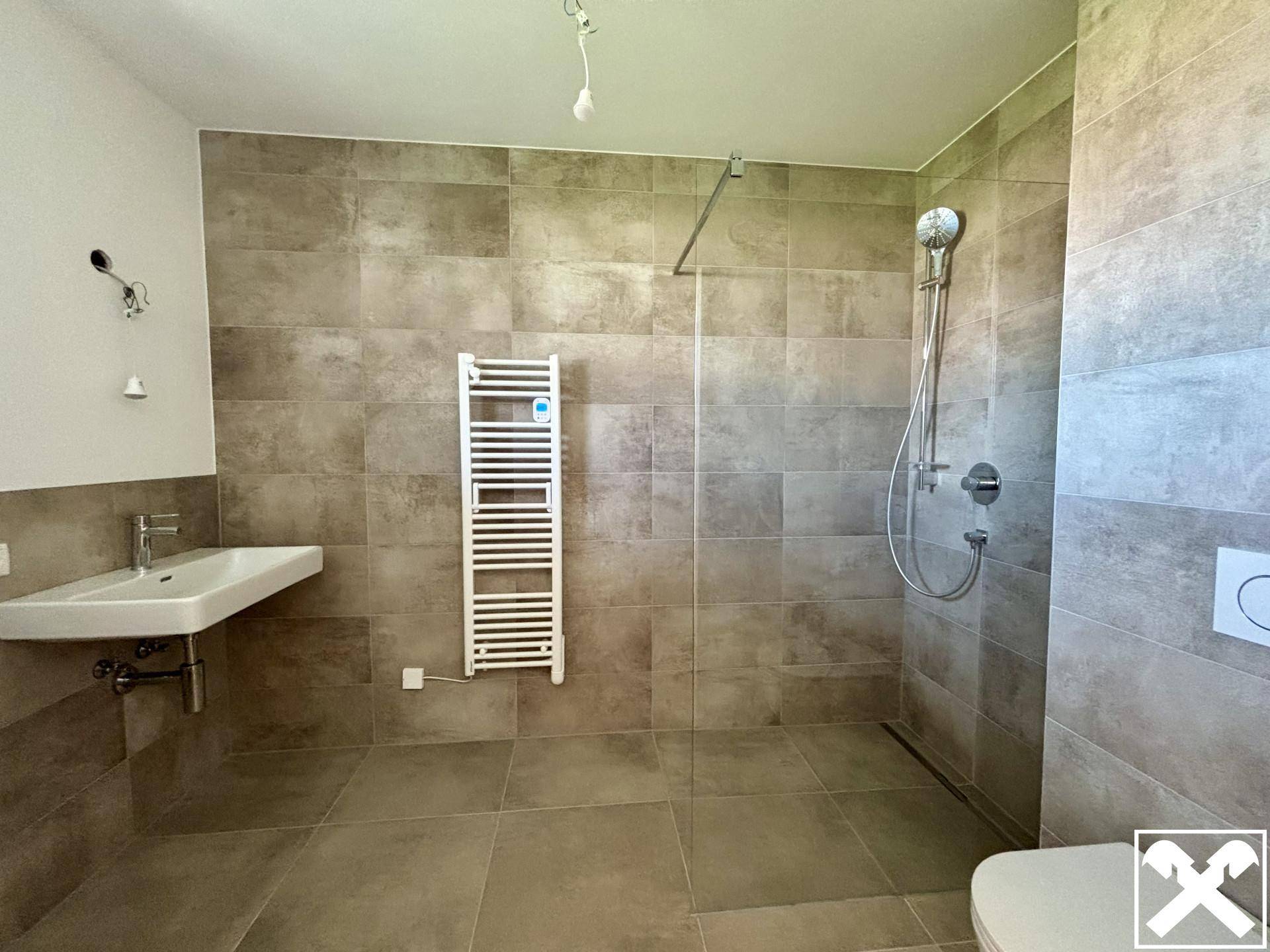 Modernes Badezimmer mit großformatigen Fliesen, ebenerdiger Dusche und beheiztem Handtuchhalter.