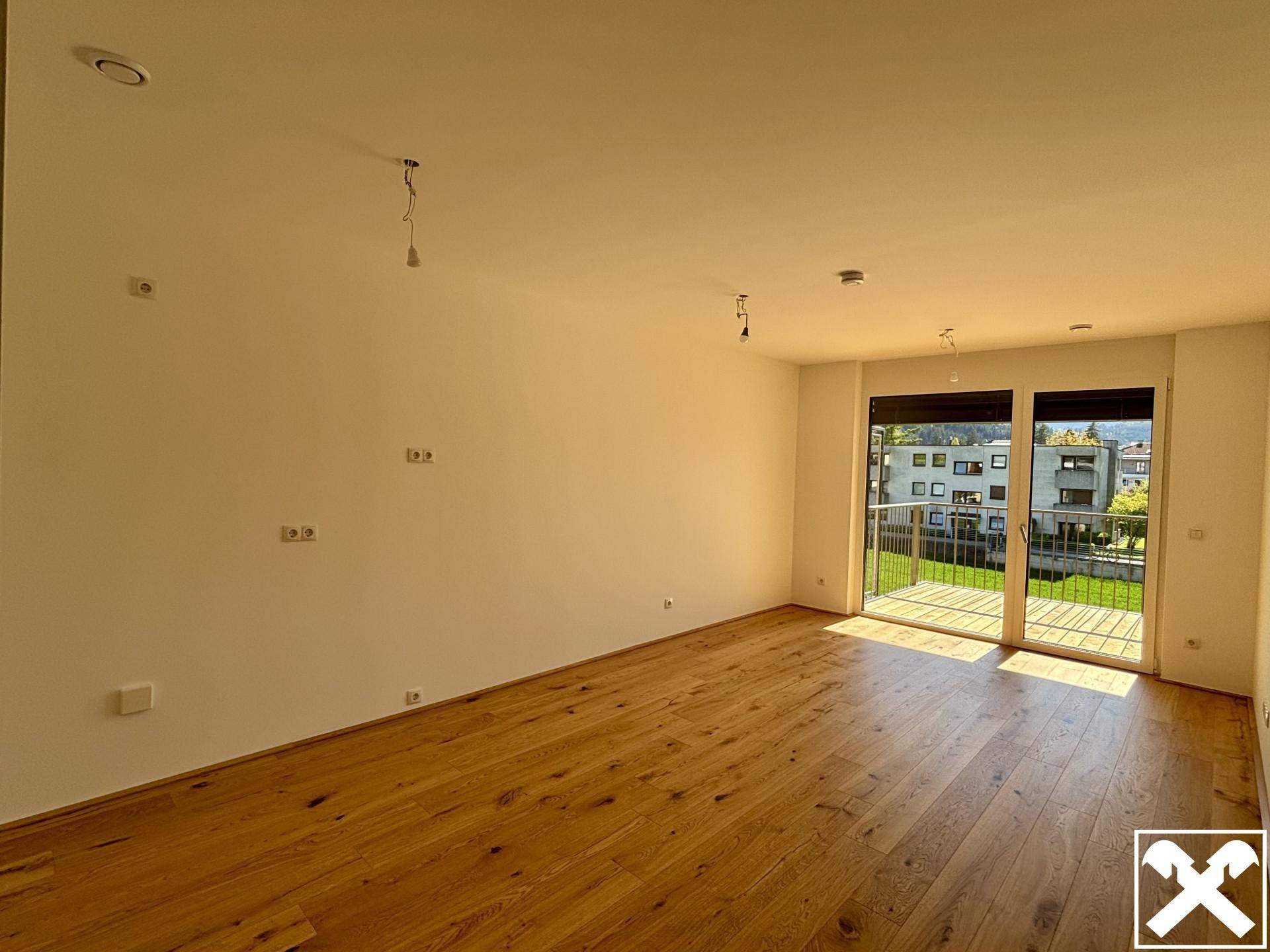 Heller Wohnraum mit hochwertigem Parkettboden und Zugang zum Balkon.