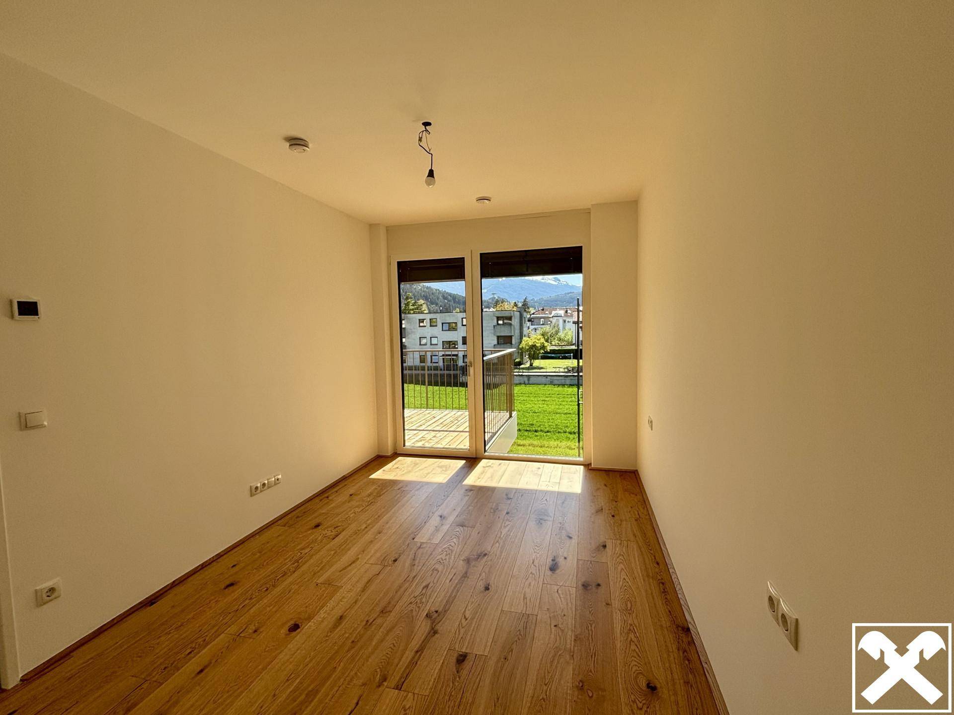 Lichtdurchfluteter Raum mit Holzboden und großen Fenstern zum Balkon.