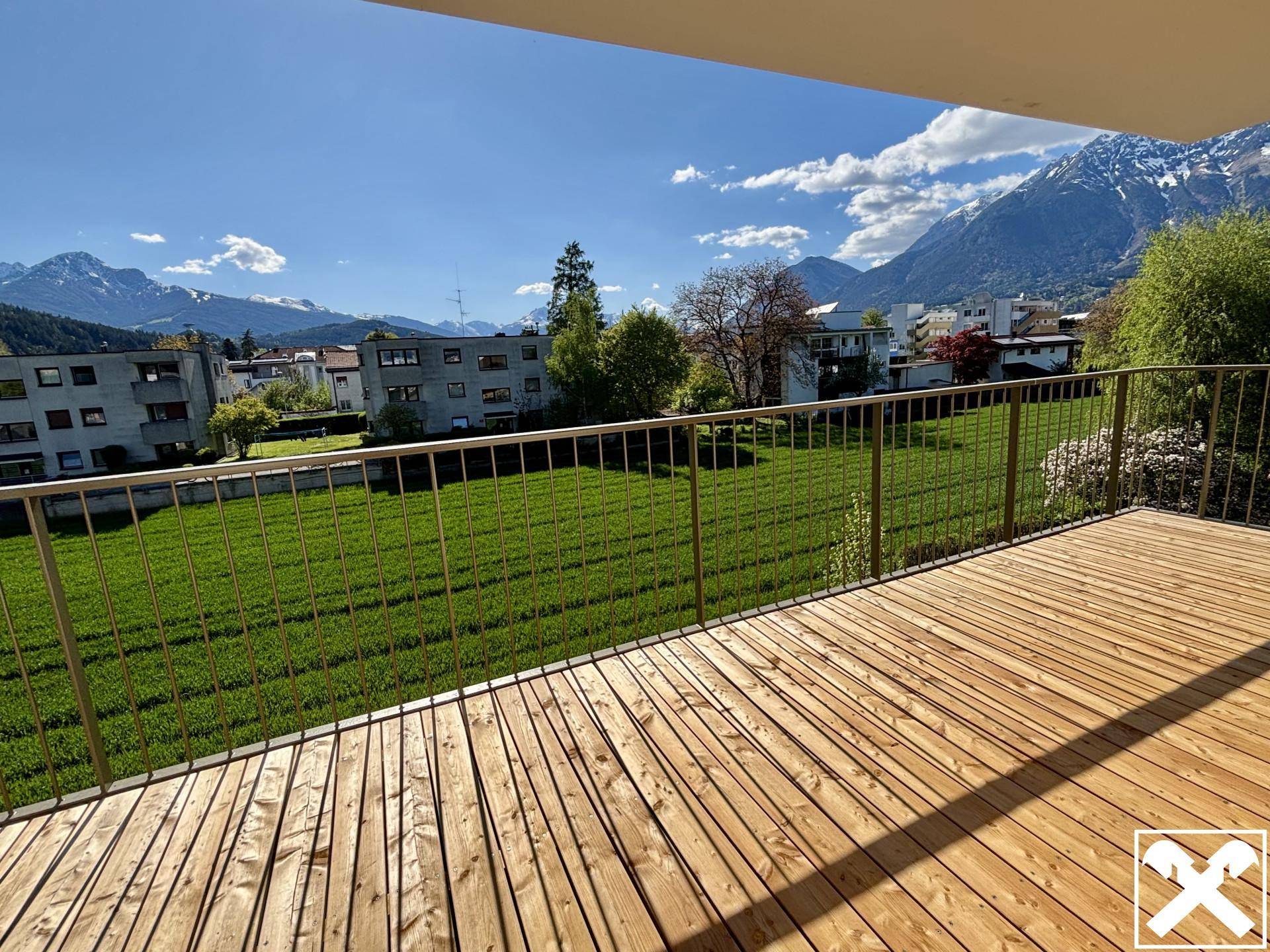 Geräumige Holzterrasse mit Blick auf grüne Wiesen und die umliegende Berglandschaft unter blauem Himmel.