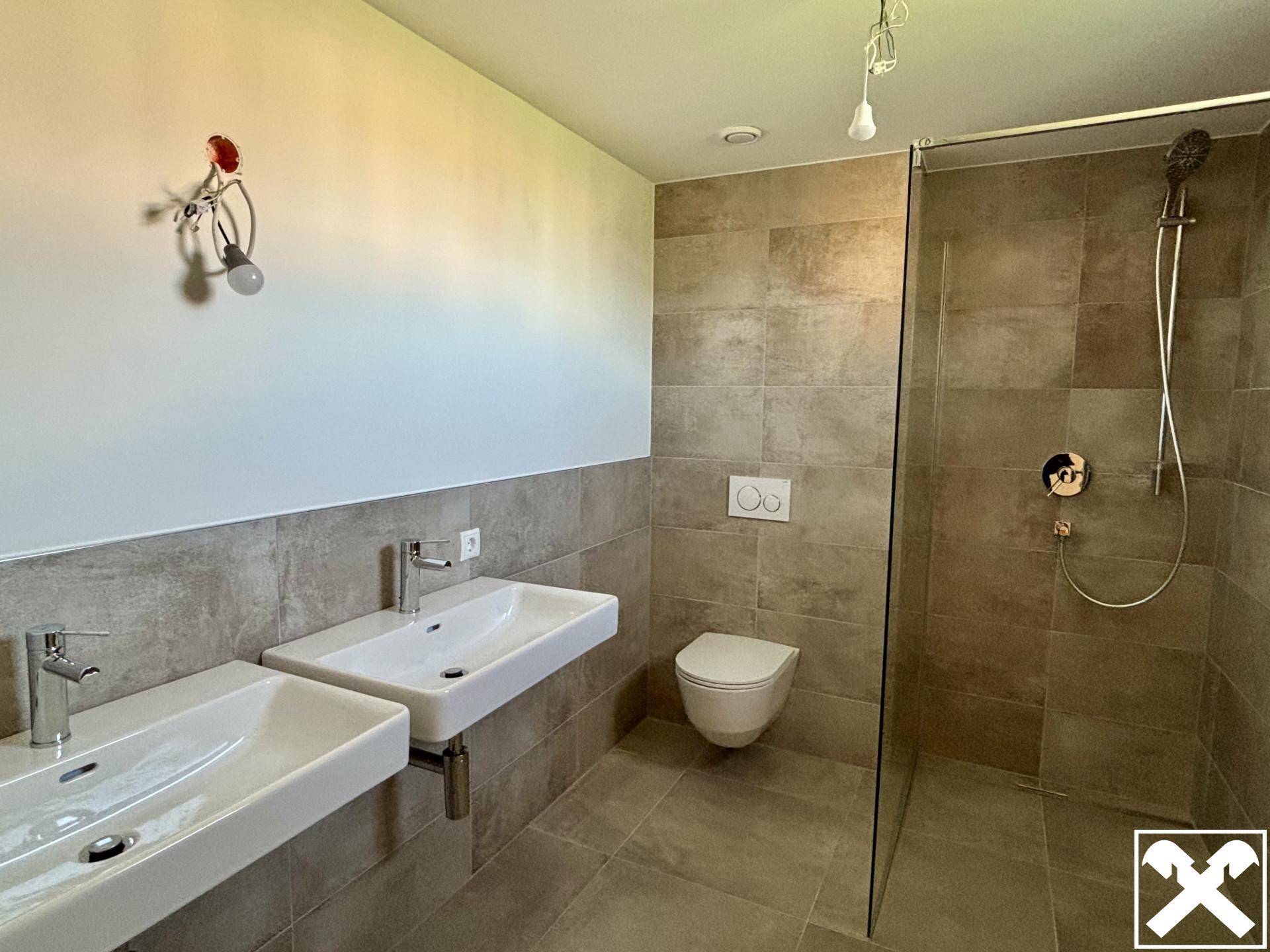 Modernes Badezimmer mit grauen Fliesen, Doppelwaschbecken und einer begehbaren Dusche mit Glaswand.