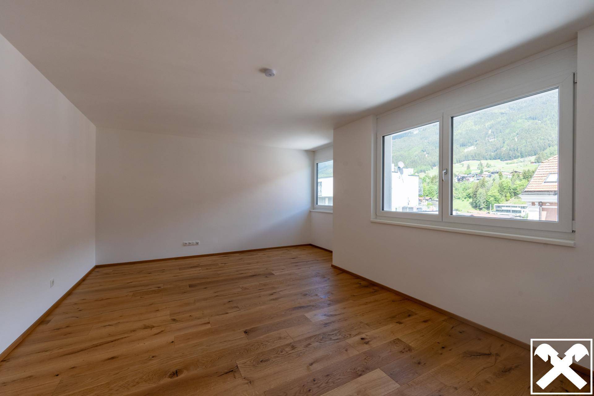 Geräumiges Zimmer mit Holzboden, großen Fenstern und Bergblick.