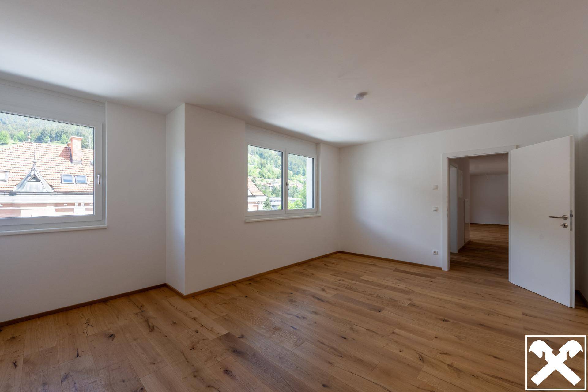 Helles Schlafzimmer mit Holzboden und Blick auf die grüne Umgebung.