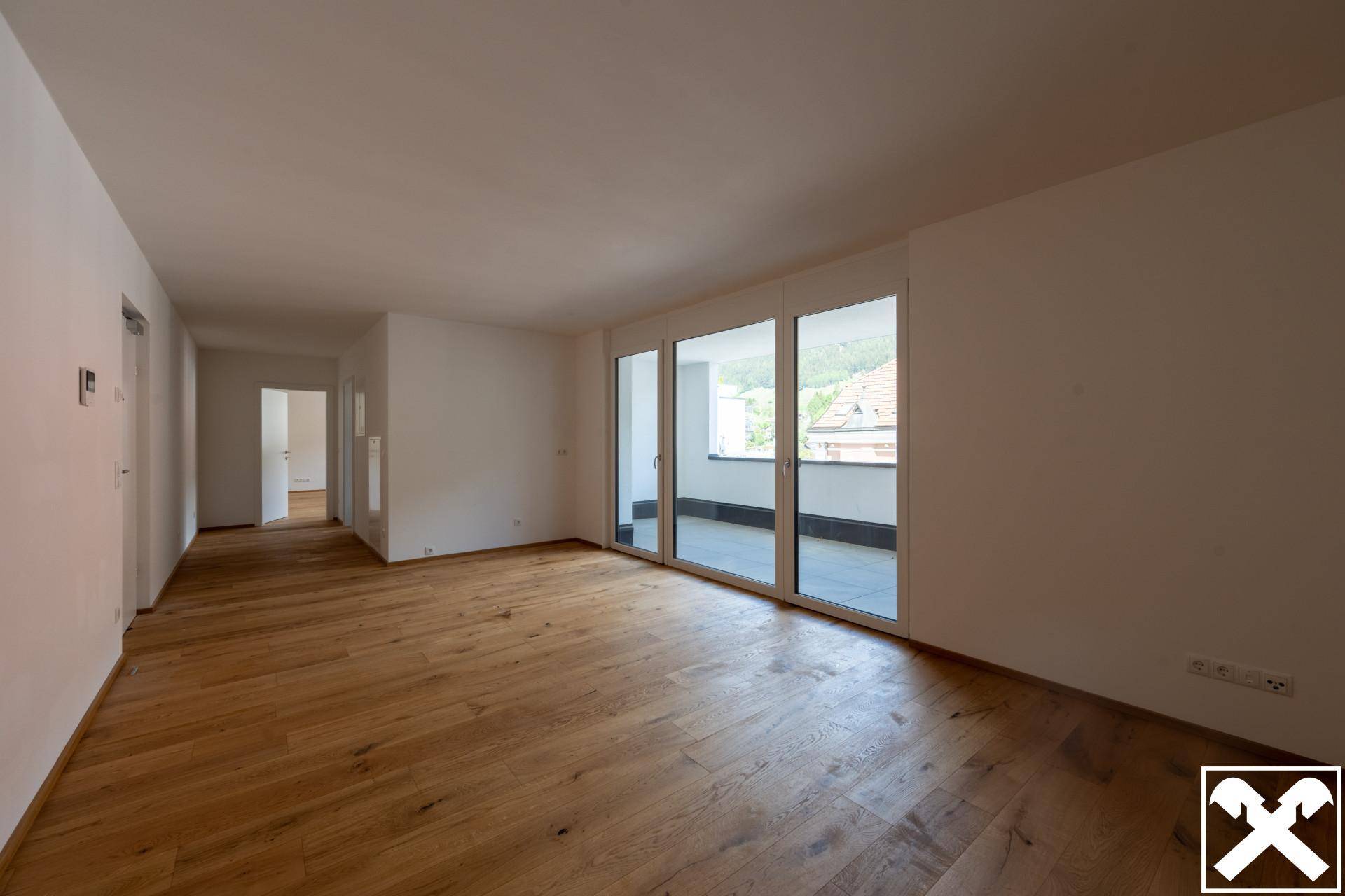 Geräumiges Wohnzimmer mit Holzboden, weißen Wänden und Zugang zu weiteren Räumen.
