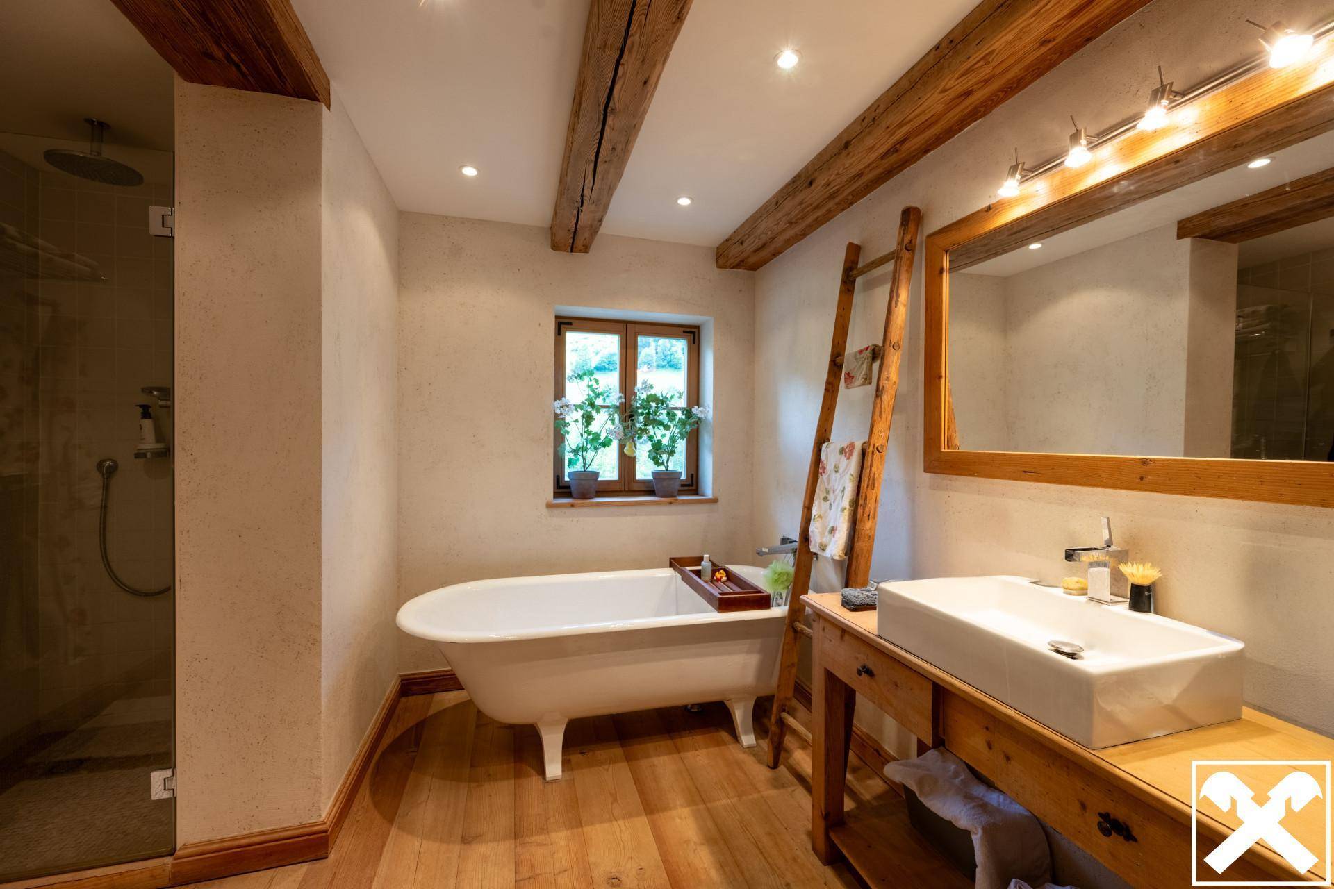 Rustikales Badezimmer mit freistehender Badewanne, Dusche und Holzbalken, strahlt Gemütlichkeit aus.