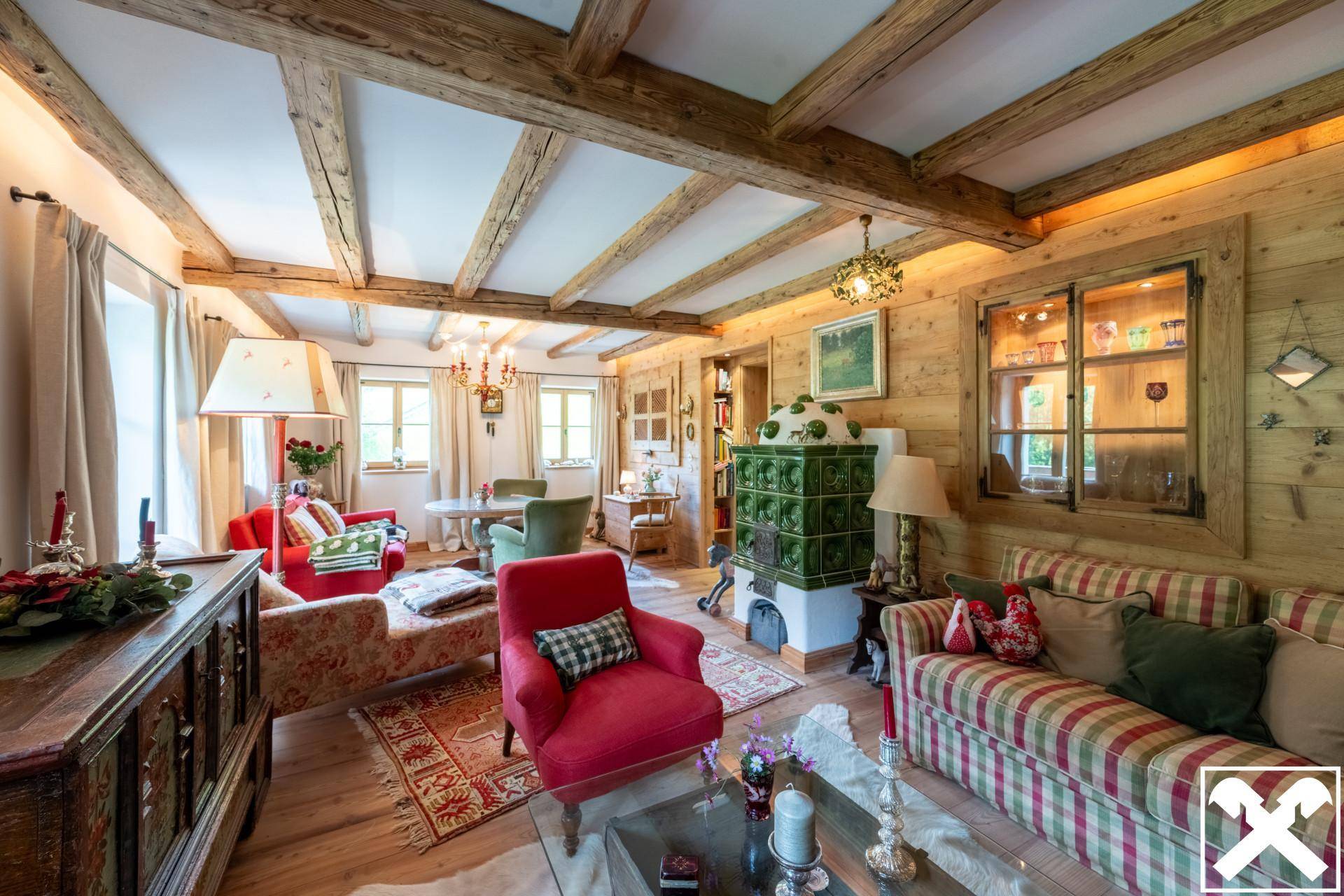 Traditionelles alpines Wohnzimmer mit Kachelofen, Holzbalken und gemütlichen Sitzgelegenheiten.