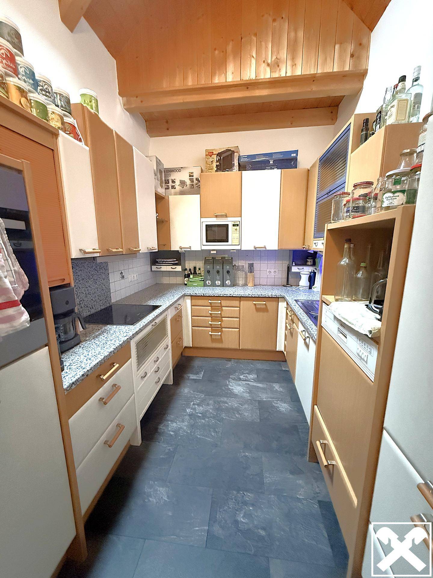 Funktionale Küche mit Holzschränken, Granit-Arbeitsplatten und integrierten Geräten.