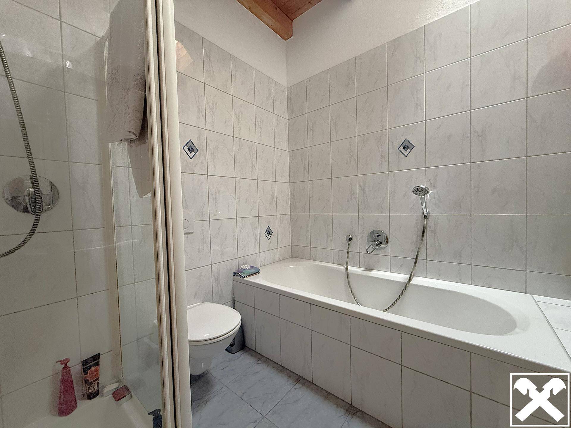 Badezimmer mit Badewanne, Duschkabine, WC und hellen Fliesen an Wänden und Boden.
