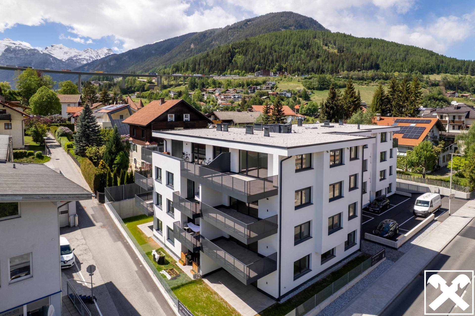 Moderne Wohnanlage in alpiner Umgebung mit Bergblick und Parkplätzen.