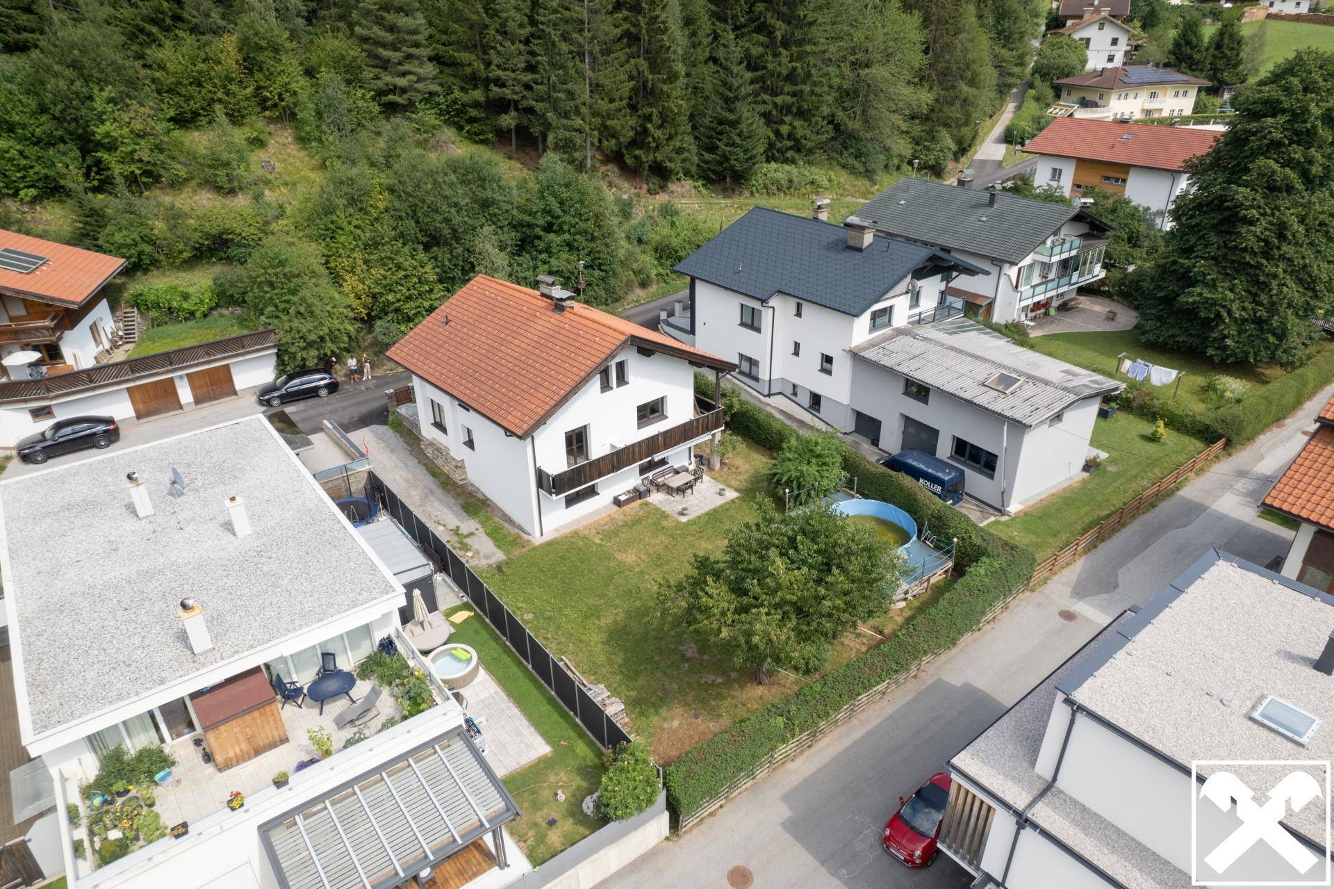 Luftaufnahme des Hauses mit Garten, Pool und umliegender Wohnsiedlung in grüner Umgebung.