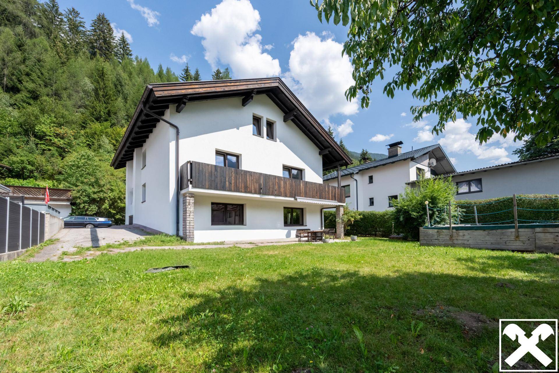 Hinteransicht des Hauses mit großem Rasenbereich, Bäumen und Bergblick.