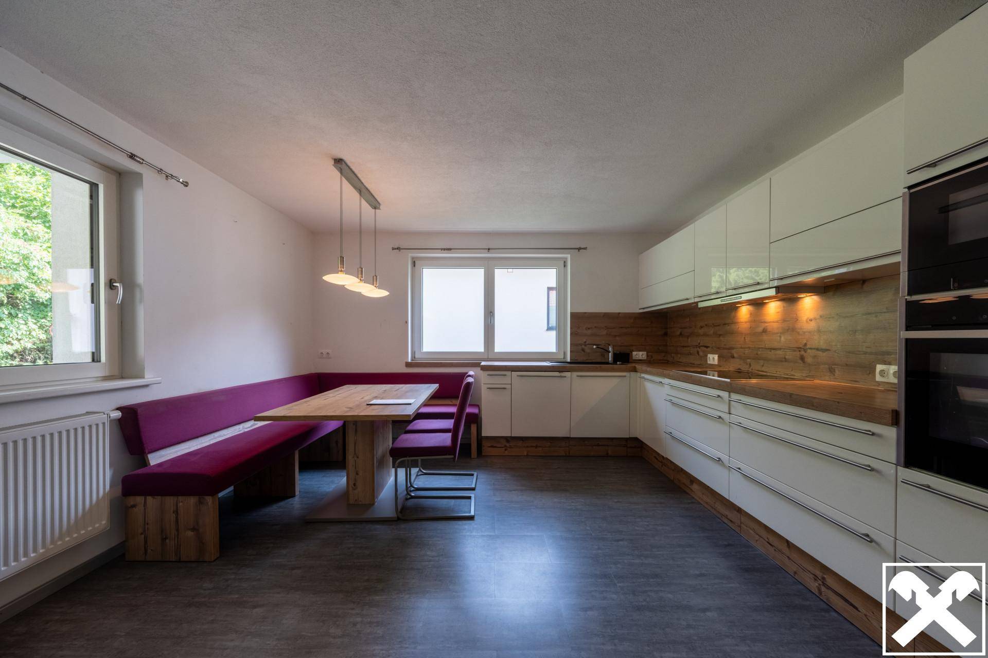 Moderne Küche mit weißen Hochglanzfronten, Holzakzenten und gemütlicher Essecke.