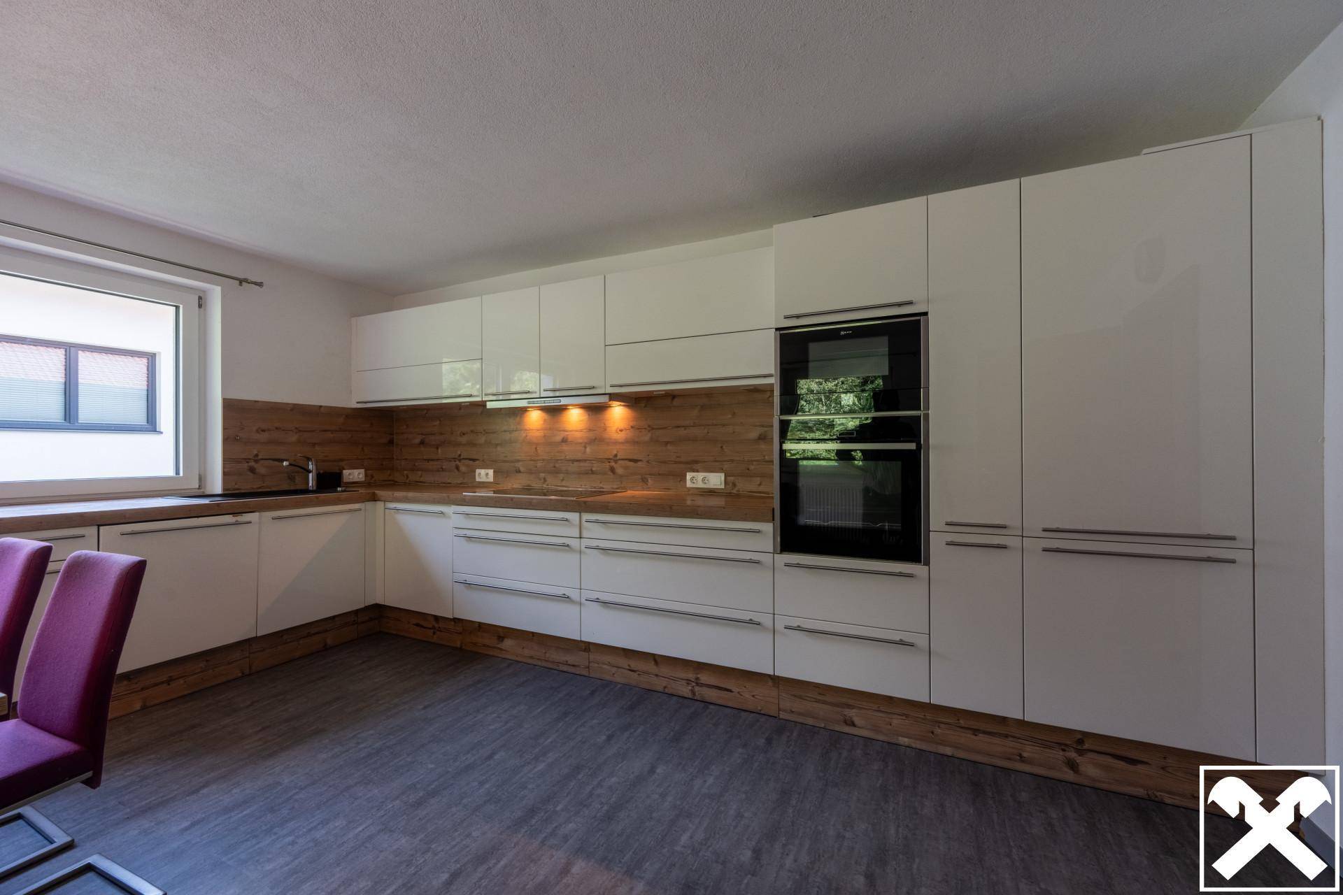 Helle Einbauküche mit weißen Schränken, Holzdetails und integrierten Elektrogeräten.