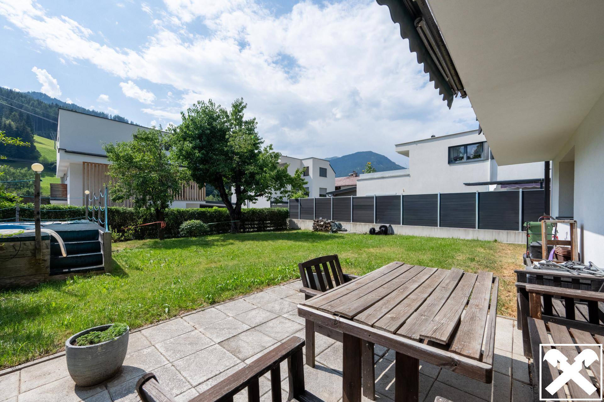 Gemütliche Terrasse mit Holztisch und Stühlen, umgeben von einem grünen Garten.