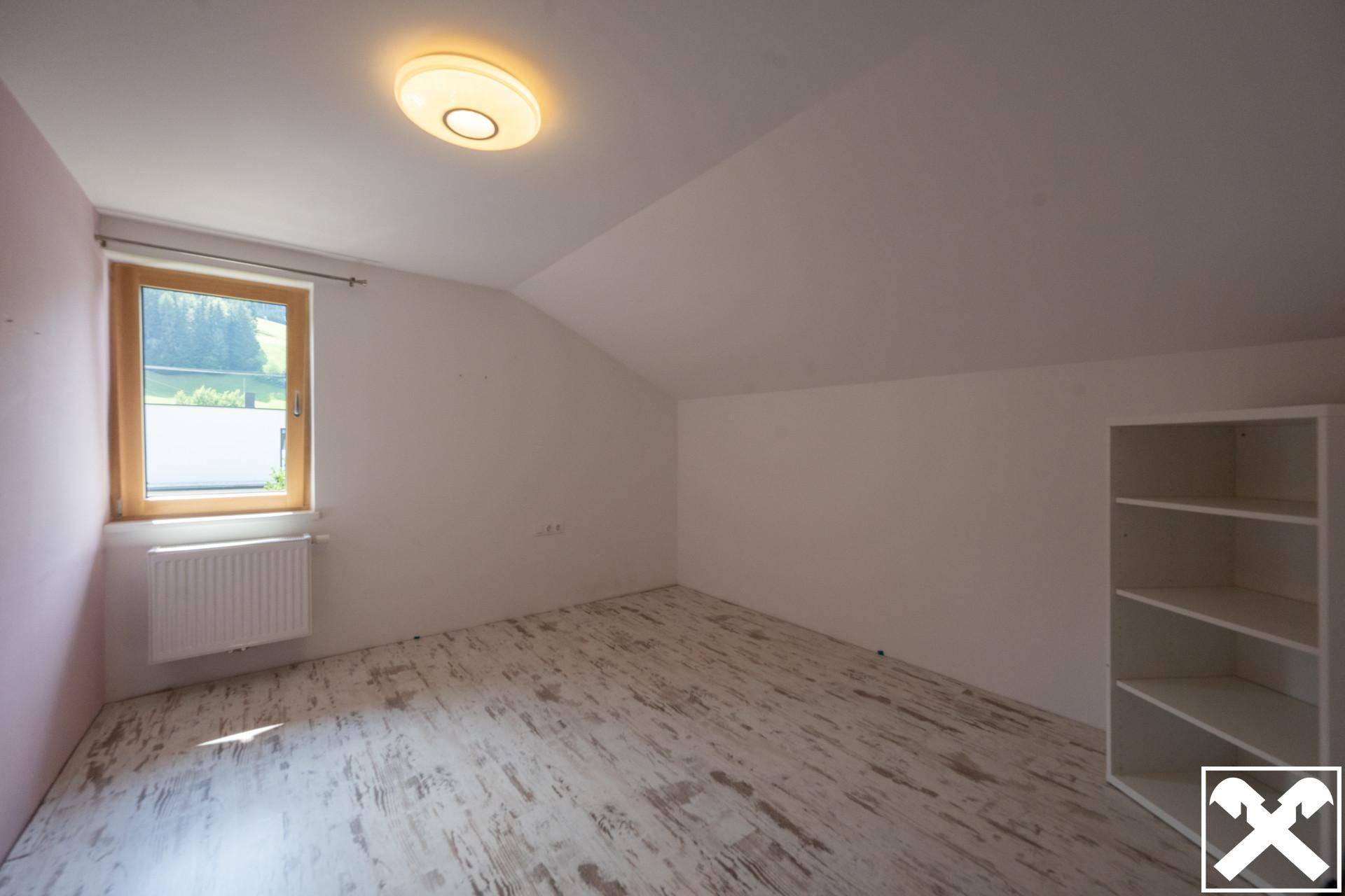 Helles Schlafzimmer im Dachgeschoss mit schräger Decke, Laminatboden und Fenster.