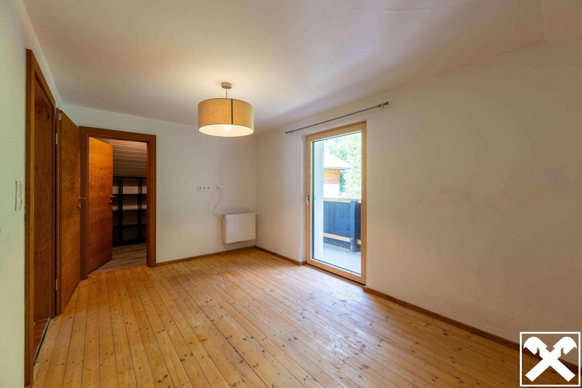 Geräumiges Schlafzimmer mit Holzdielenboden und direktem Zugang zum Balkon.
