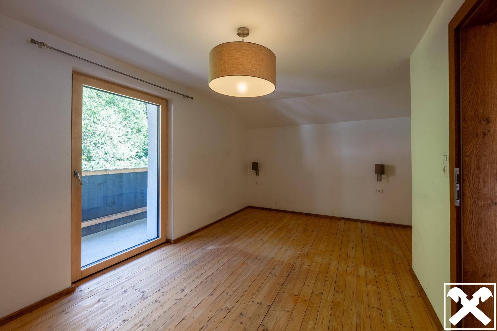 Helles Schlafzimmer mit Holzdielenboden, Balkonzugang und Blick ins Grüne.
